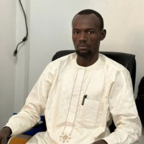 Mr. Tahir Sidick Oume, wearing a white traditional robe and seated in a black office chair